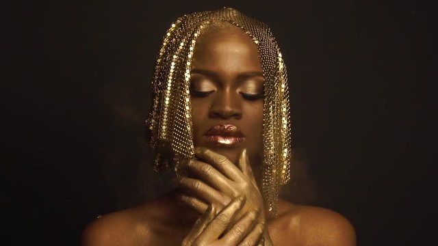 Enigmatic magic african american female model with golden glossy makeup and headwear posing for camera. High fashion Vogue concept
