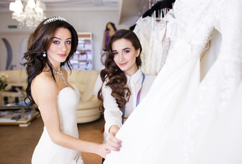 Naklejka premium Female trying on wedding dress in a shop with women assistant.