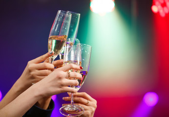 Clinking glasses of champagne in hands on bright lights backgrou