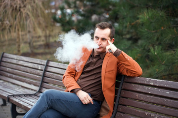 Fototapeta premium A young man sits on a bench and smokes an electronic cigarette.