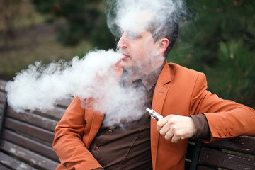 Obraz premium A young man sits on a bench and smokes an electronic cigarette.