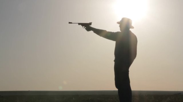 Silhouette of a cowboy shooting a pistol on a background of the rising sun
