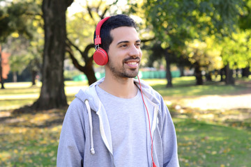 Naklejka na ściany i meble Young man listening to music with headphones in park.