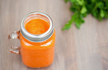 Healthy carrot smoothie in a jar with tube and parsley on wooden background. Shallow dof