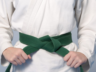 Hände, die den grünen Gürtel an einem Teenager im Kimono für Kampfkünste anziehen