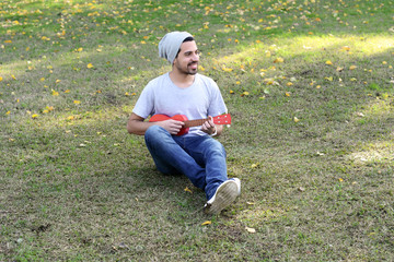 Naklejka na ściany i meble Young man playing the ukelele in a park.