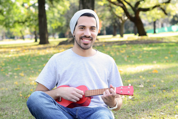 Obraz premium Young man playing the ukelele in a park.