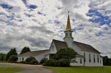 Church building with steeple and belfry against a partly cloudy summer sky