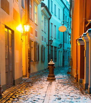 First Snow In Narrow Medieval Street In Old Riga, Latvia.  Riga Is The Capital And Largest City Of Latvia, A Major Cultural, Historical, Tourist And Financial Center Of The Baltic Region