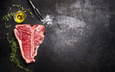 Raw T-bone Steak with fresh herbs and oil on dark rust metal background, top view, place for text,...