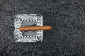 Glass ashtray and cigar on a black natural leather