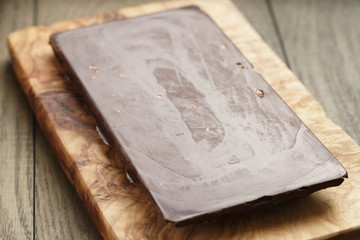 whole homemade bar of chocolate with cashew nuts, on wooden board shalow focus