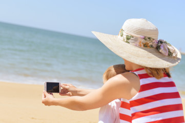 Female with child taking selfie at tropical beach on sunny outdoors background