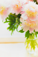 Lovely pink pale peonies  in glass vase on light background, close up