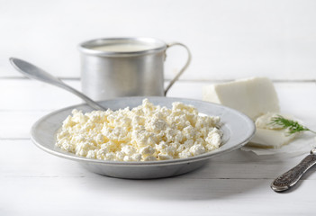 Plate of homemade cottage cheese, served with vintage aluminum pan , cheese milk and knife on a white wooden background. rustic style