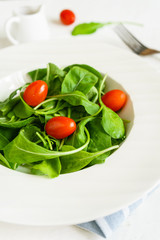 Rocket salad with cherry tomatoes on white wooden background