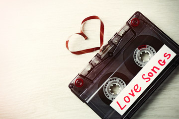 Retro audio cassette with tape in shape of heart on wooden background