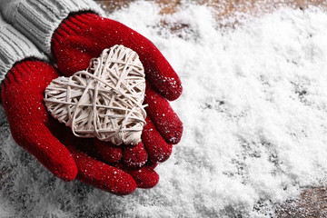 Female hands in mittens with decorative heart on snow background