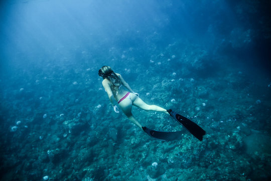 Woman in bikini and fins swims along the bottom of the ocean