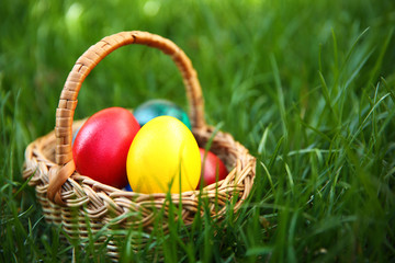 Basket with coloured Easter eggs on green grass