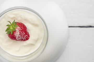 Single strawberry with sugar, cream or yogurt as a sweet dessert in glasses ball on wooden light blue table