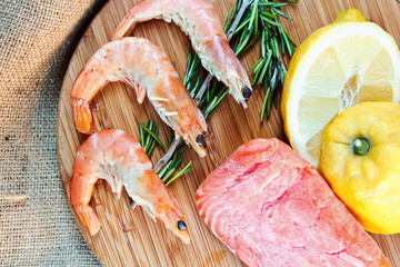 Raw salmon and shrimps with rosemary and lemon on the wooden board