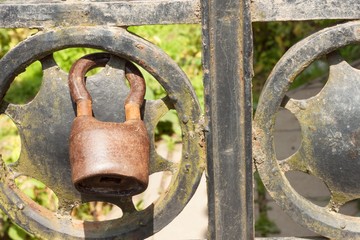 Old rusty lock on a metal gate into the garden. Lock on the iron gate. Symbol imprisonment and slavery. Property security chain. Closed iron gate with a lock. Safe lock. 
