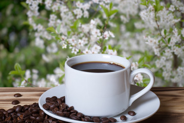 Coffee beans and coffee in white cup on wooden table opposite a