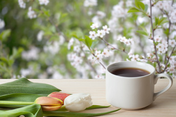 Coffee in a cup and tulips on wooden table opposite a defocused