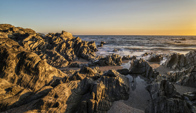 Beautiful vibrant sunset landscape image of calm sea against roc
