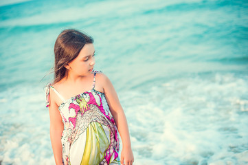 Child walking along the seacoast. Girl in a colorful dress walking on the beach