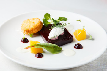Beetroot terrine, goat cheese croquettes, horseradish sauce and dill cream on white dish
