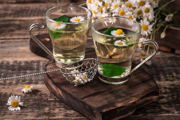 herbal chamomile tea on a wooden table. Chamomile tea in a transparent cup and camomile flowers on wooden table. Herbal tea for baby's stomach. Copy space.
