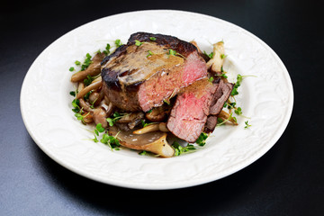 Tasty Beef Mignon steak with mushrooms and herbs on plate.