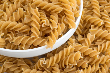 Fusilli whole wheat organic pasta in a white bowl surrounded by more spiral pasta.