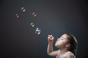 Lovely little girl blowing soap bubbles on dark background