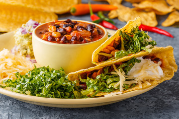 Tacos with chili con carne, salad, cheese and sour cream.