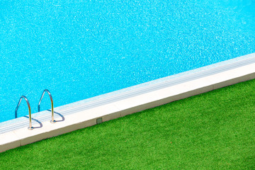 Infinity pool on the bright summer day with green grass around.Swimming pool with stairs into the water.Hotel swimming pool with sunny reflections close up view.