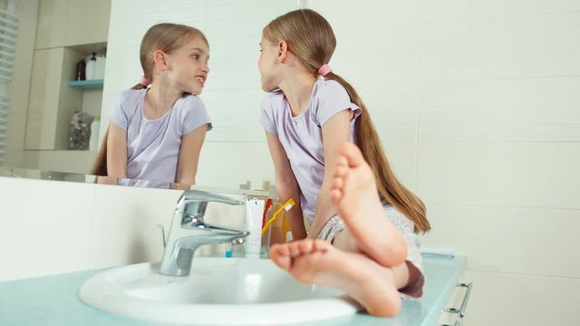 Portrait blonde child girl 7-8 years sitting in the bathroom and viewing her teeth