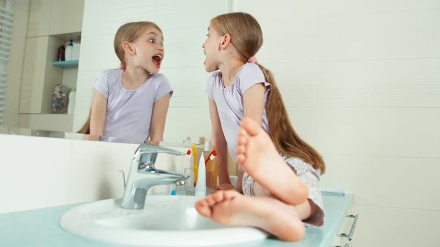 Portrait blonde child girl 7-8 years sitting in the bathroom and viewing her teeth and and uses the toothbrush