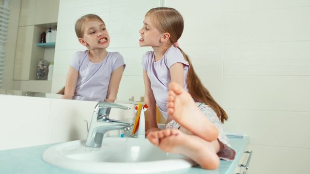 Portrait cute girl sitting near a mirror in the bathroom and viewing her teeth and using toothbrus