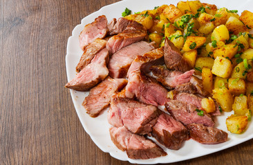 Sliced medium rare grilled Steak Ribeye with potato in a plate on wooden table
