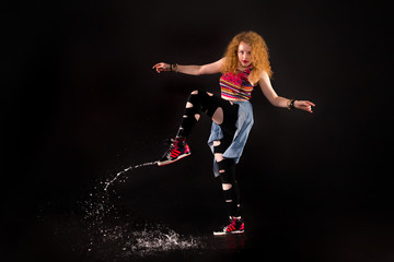 red-haired girl in a street style lifted her leg in a dance with splashes. studio with black background