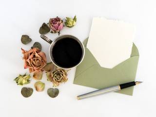 Cup of coffee, blank paper in the envelope, pen and flowers. flat lay, top view