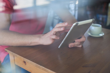 The hand of a man sitting at a table in a cafe holding a tablet and clicks on the screen