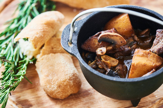 Ragout of veal with mushrooms, sauce demiglas in an iron pot and crusty bread on a wooden plate