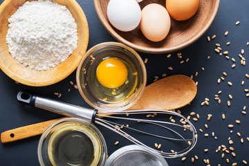 Baking ingredients. Bowl, eggs, flour, eggbeater, rolling pin and eggshells on black chalkboard from above.