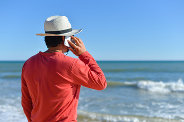 Back view of person on sunny beach outdoors talking smartphone. Vacation holiday