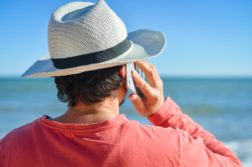 Person talking on cell phone looking at open water blue sky horizon, sunlight outdoors background.