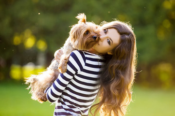 Beautiful girl in a striped sweater smiles and holds a small dog